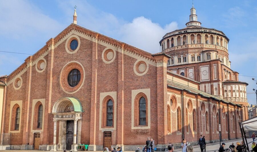 Santa Maria delle Grazie with a round tower and people walking around